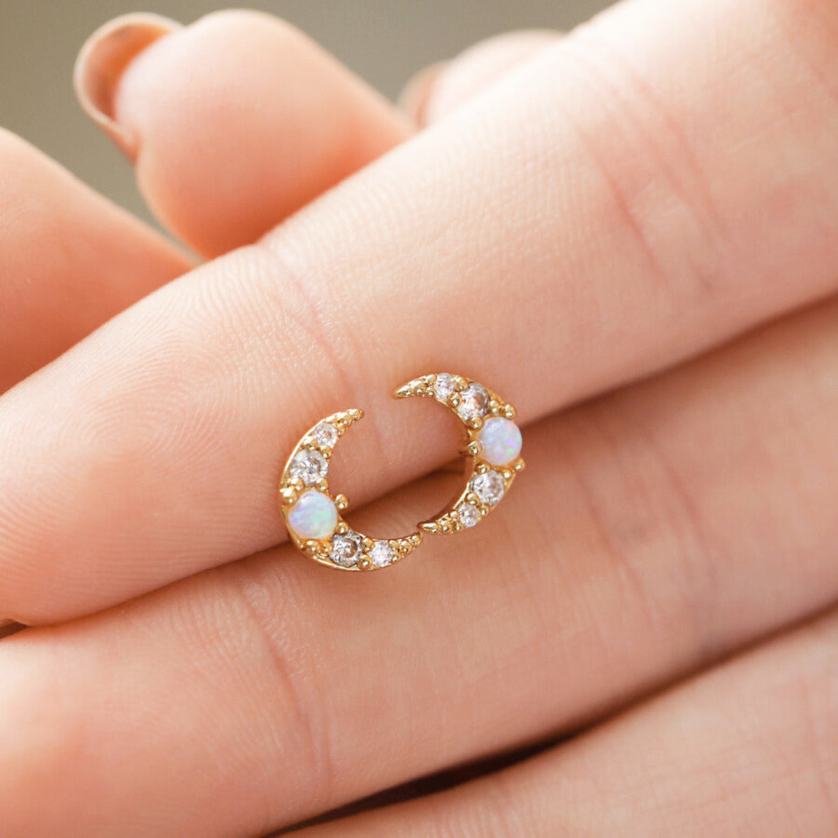 A pair of Opal Crescent Moon Studs in Gold held in a hand