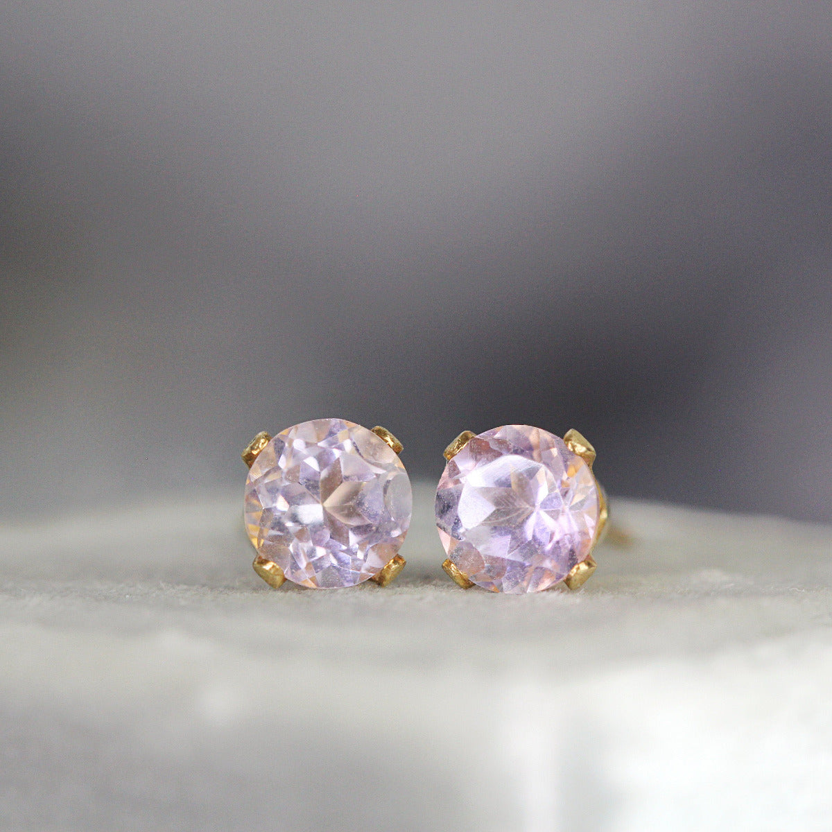 One pair of matching gemstone stud earrings in gold settings. The amethyst gemstone is round, faceted, sparkling and pale lavender purple in colour. The stones are set into 14k gold fill ear posts with a 4 prong setting with matching butterfly backs.