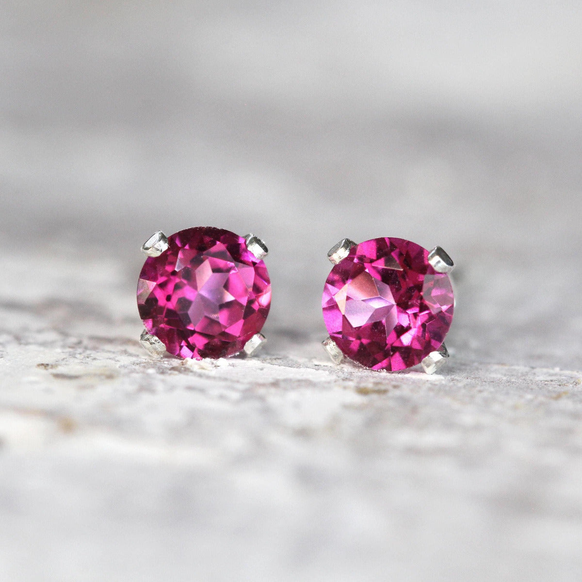 A simple minimal pair of stud earrings featuring faceted, sparkling, bright pink topaz gemstones set into a sterling silver prong setting. The earrings are a brilliant round cut, with ear post fitting and butterfly backs. Available in various sizes.