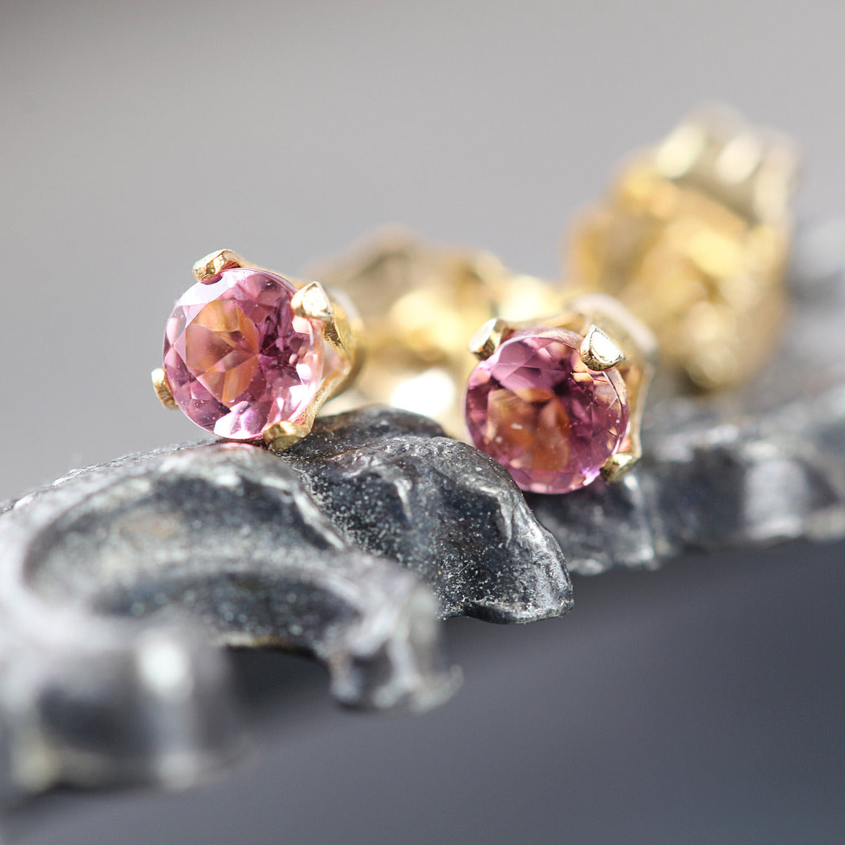 A pair of pink tourmaline stud earrings. The tourmaline stone is round in shape with a facted cut. The 14k gold fill ear post setting has four prongs holding the gemstone in place, and butterfly push backs to hold the stud securely on the ear.