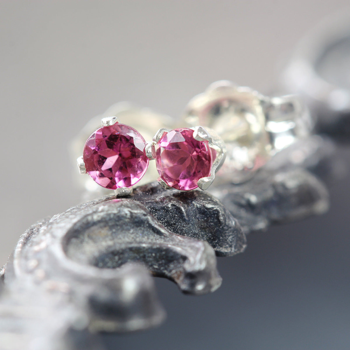 A pair of deep rose pink gemstone stud earrings. The tourmaline gemstones are sparkling and catch the light. The stones are a brilliant round cut with lots of facets, and set into sterling silver four prong settings. Simple, minimal stud earrings.