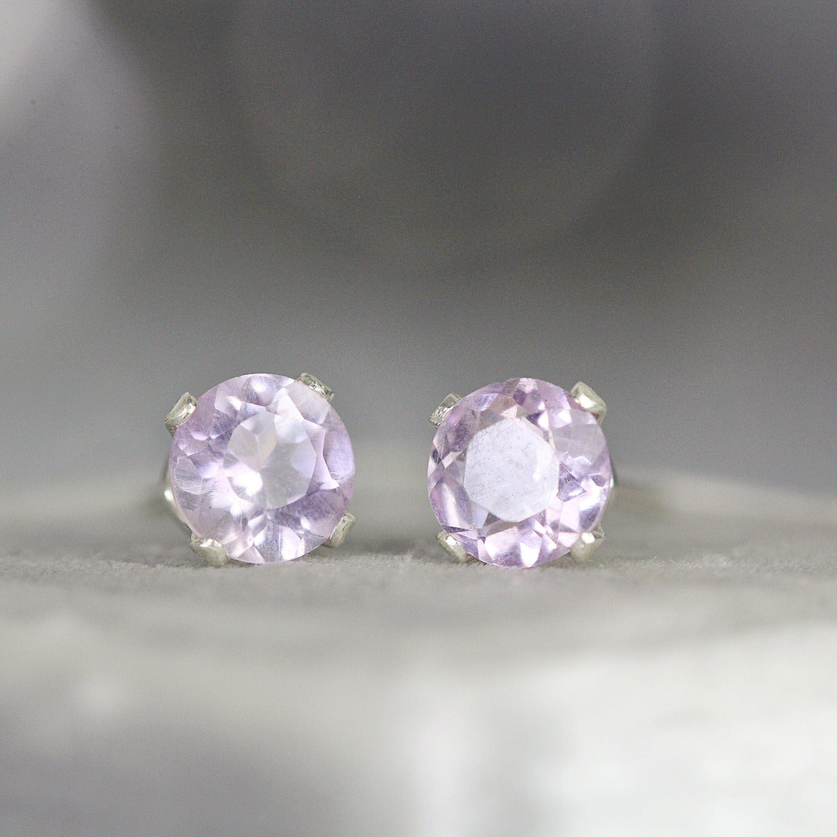A pair of light purple amethyst stud earrings. The amethyst gemstones are sparkling and catch the light. The stones are a brilliant round cut with lots of facets, and set into sterling silver prong settings. Simple, minimal, round stud earrings.