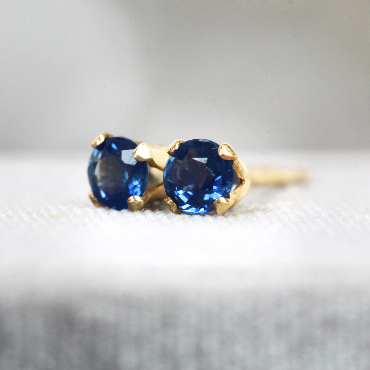 Gold stud earrings with blue sapphire gemstones on a light gray background