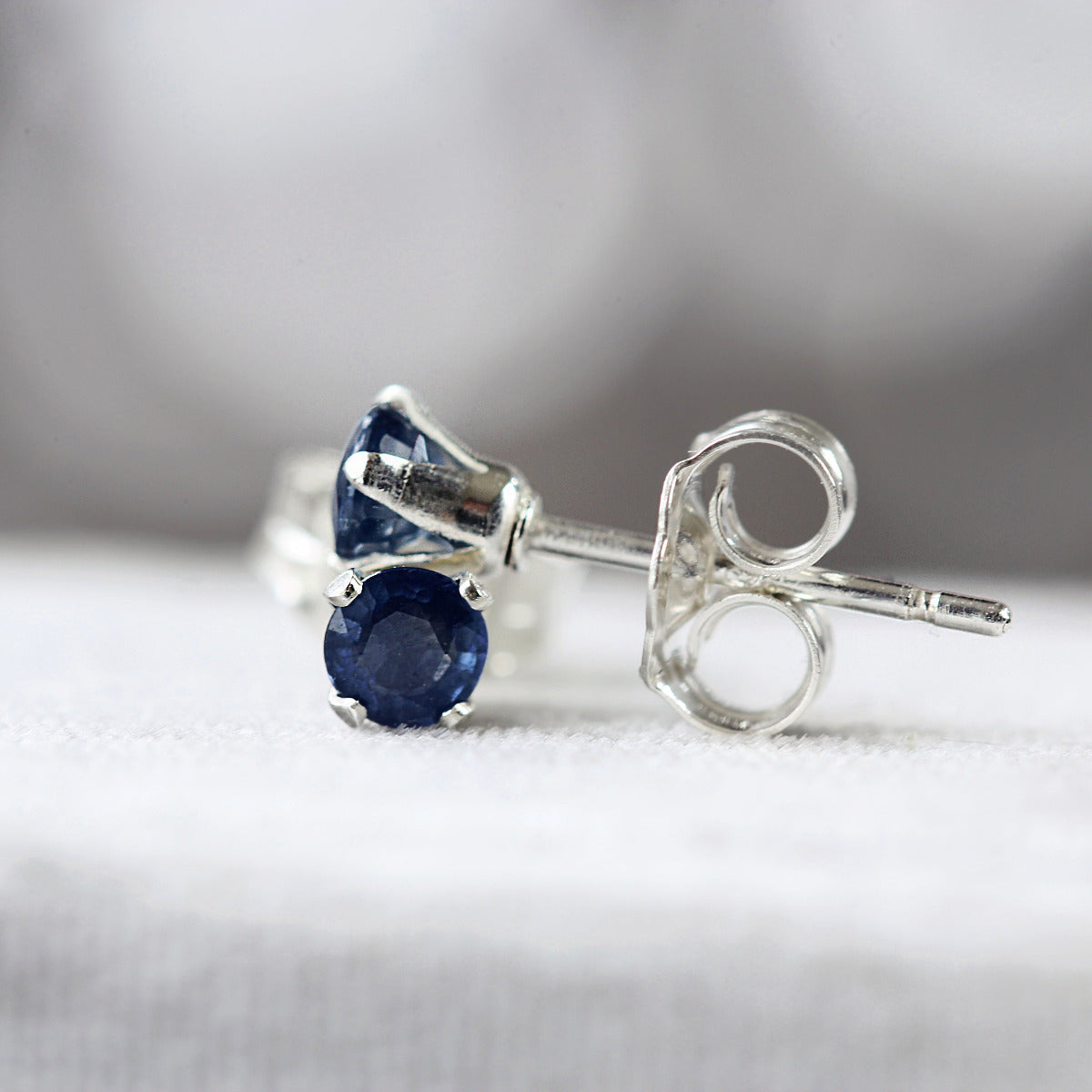 Silver stud earrings with deep blue sapphire gemstones on a white background