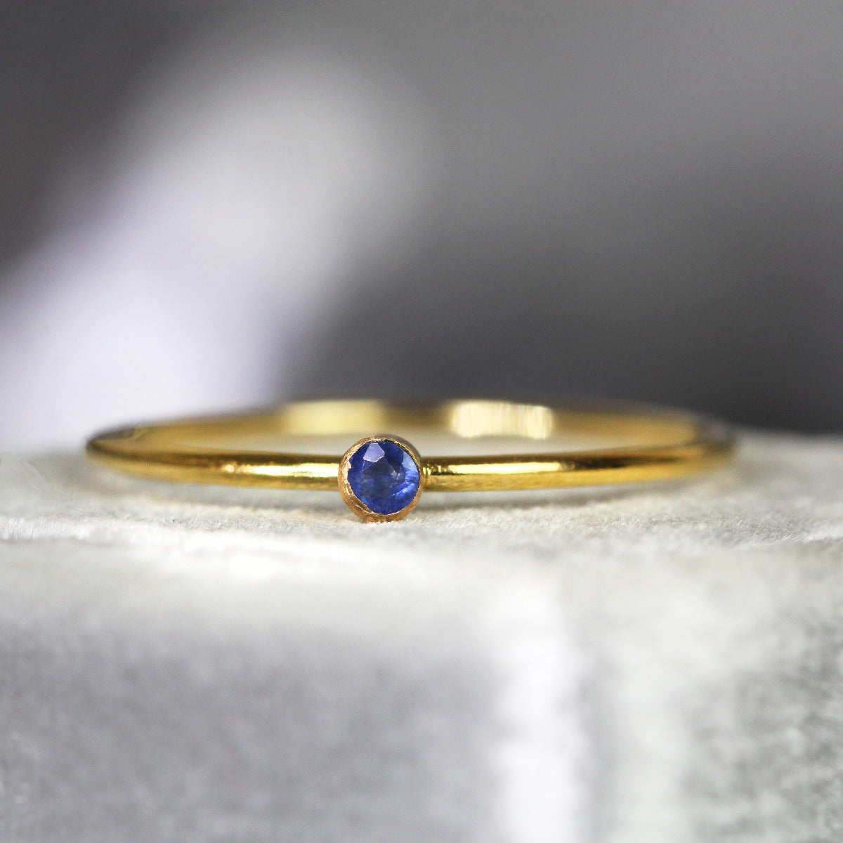 Minimal gold ring with a blue sapphire gemstone on a textured surface
