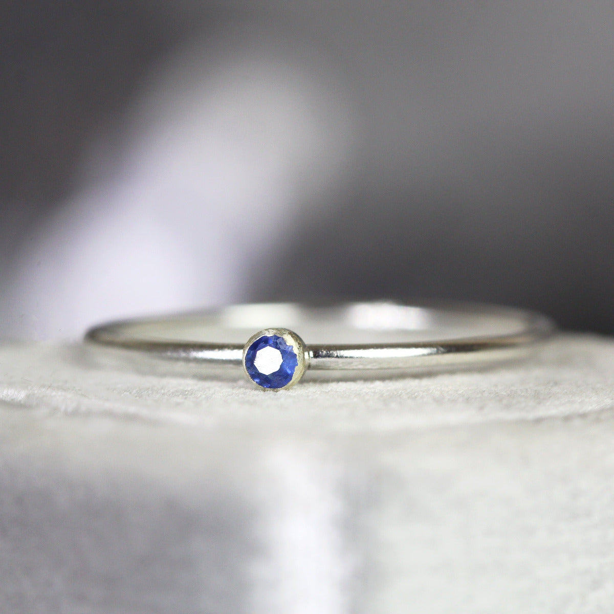 Minimalist silver ring with a blue sapphire gemstone on a textured surface