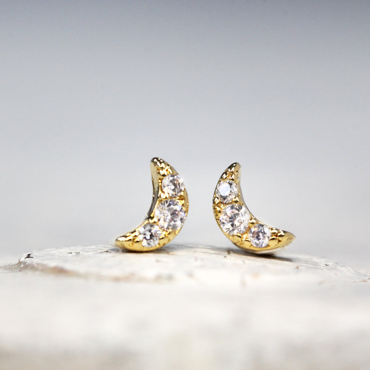A pair of Small gold moon studs with crystals on a white background