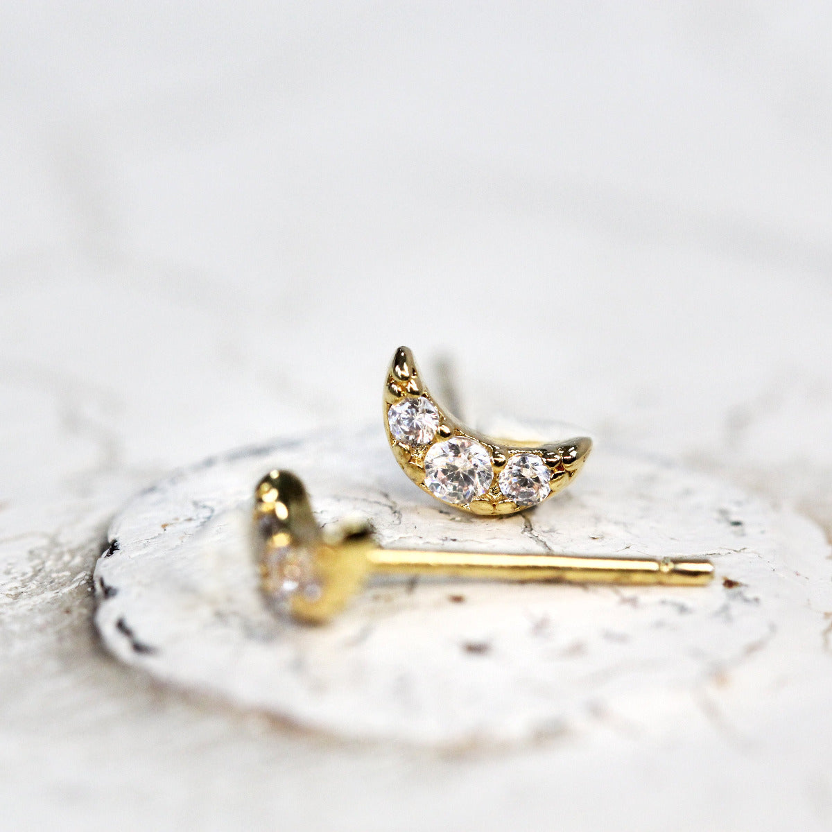 Tiny moon shaped stud earrings with crystals set into gold.