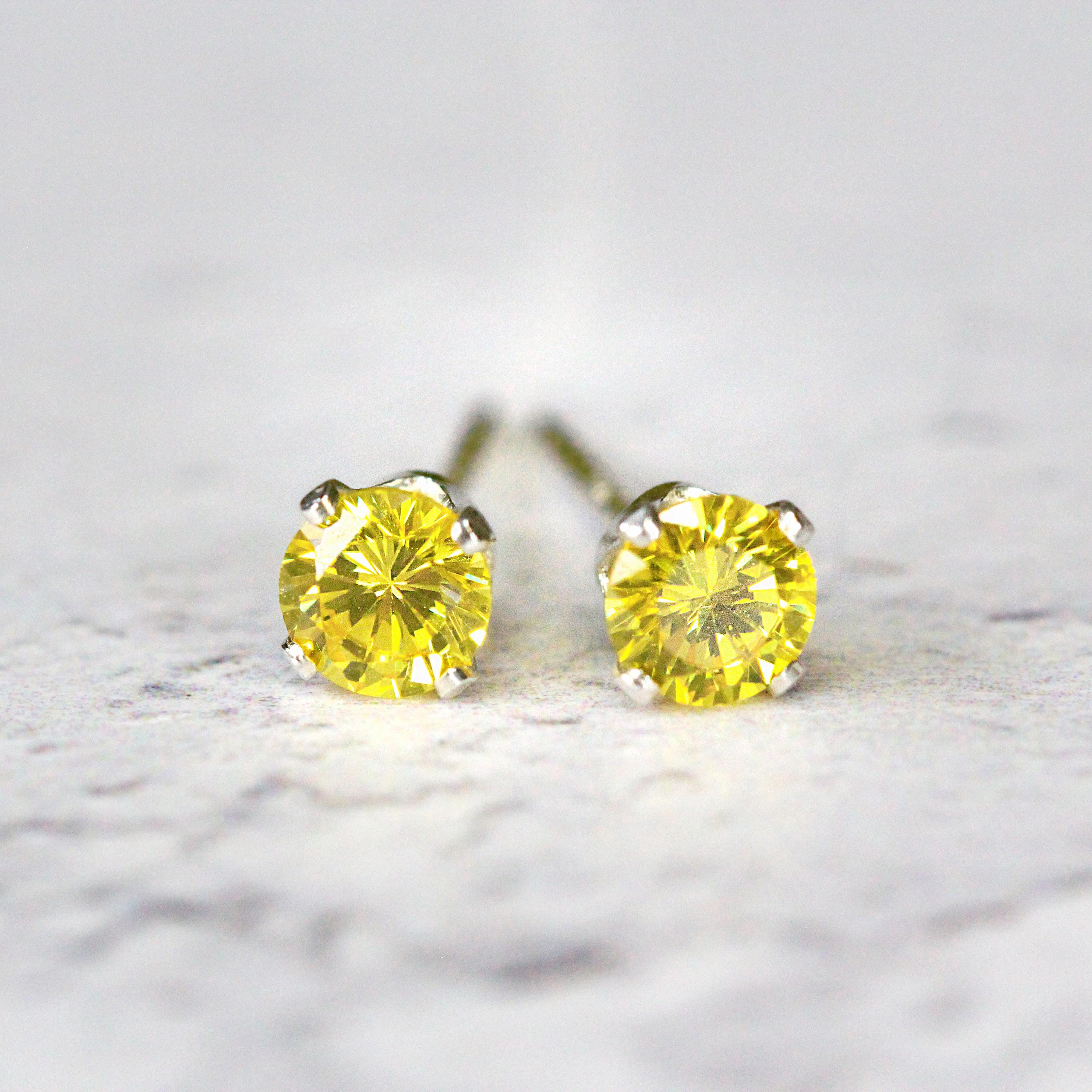 A pair of yellow cubic zirconia stud earrings. The cz gemstones are sparkling and catch the light. The stones are a brilliant round cut with lots of facets, and set into sterling silver four prong settings. Simple, minimal, round stud earrings.