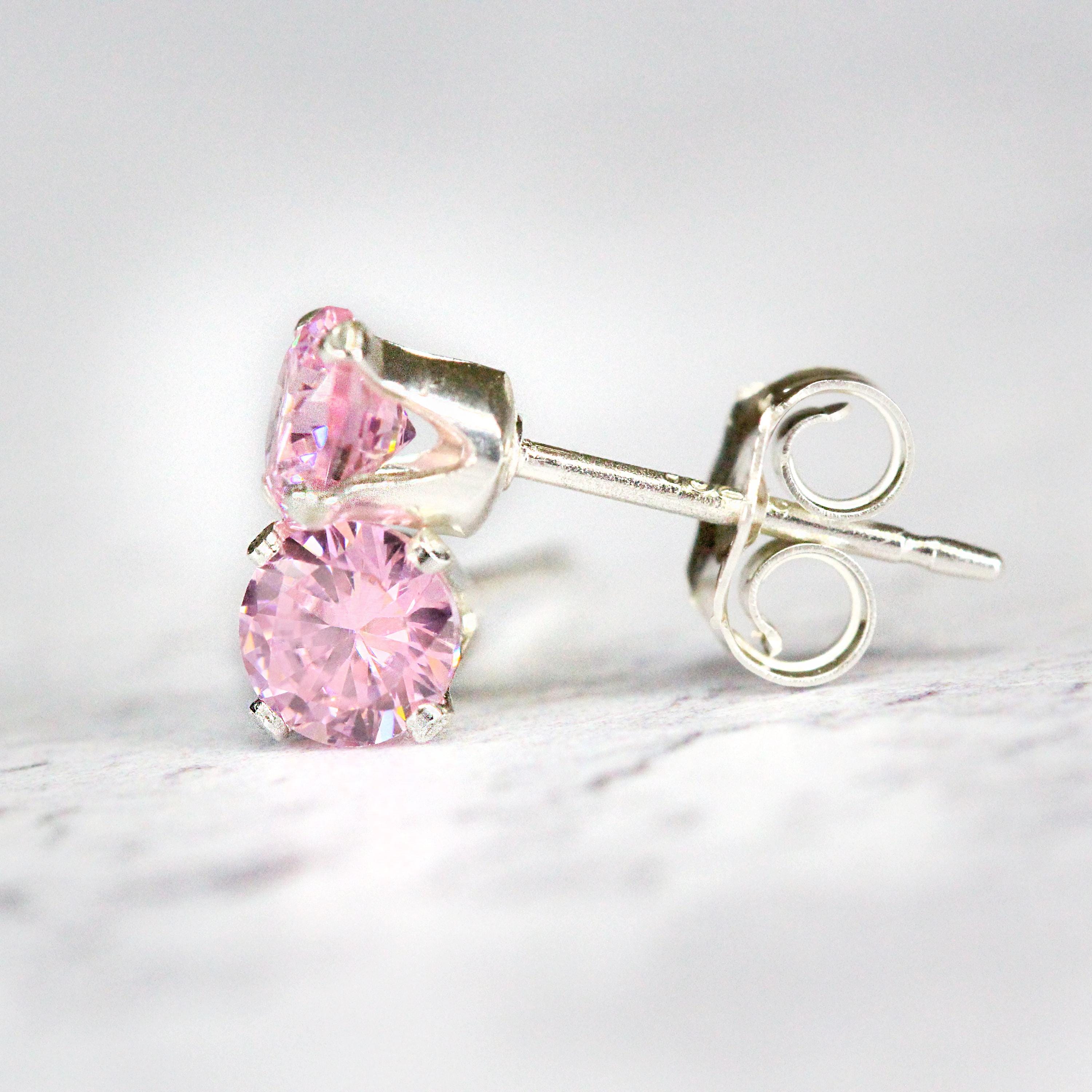 A pair of rose pink cubic zirconia crystal gemstone stud earrings. The cz gemstones are sparkling and catch the light. The stones are a brilliant round cut with lots of facets, and set into sterling silver four prong settings. Simple, minimal, round stud earrings shown against a simple light background.