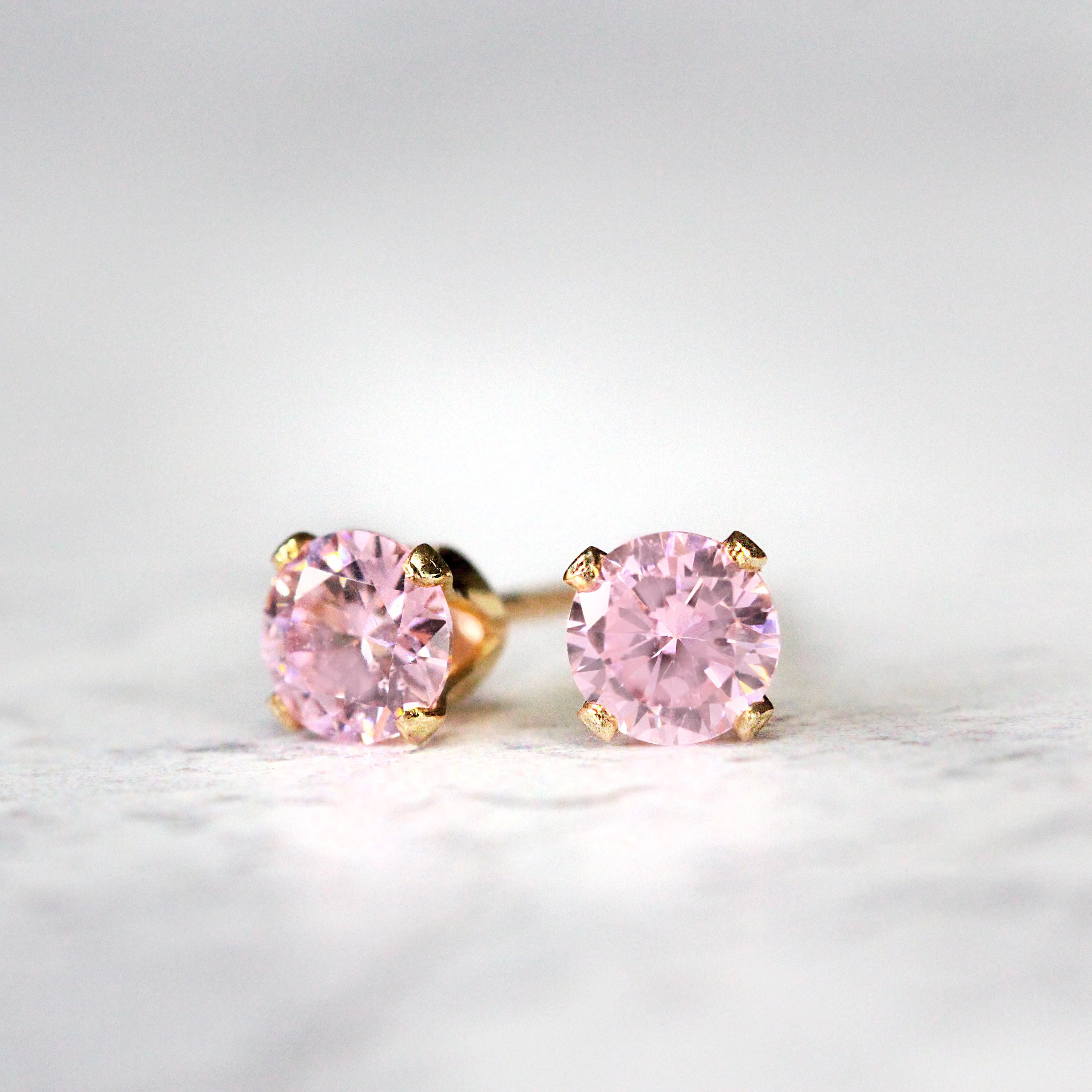 A pair of pink cubic zirconia stud earrings. The cz stone is round in shape with a sparkling faceted cut. The 14k gold fill ear post setting has four prongs holding the gemstone in place, and butterfly push backs to secure the stud on the ear.