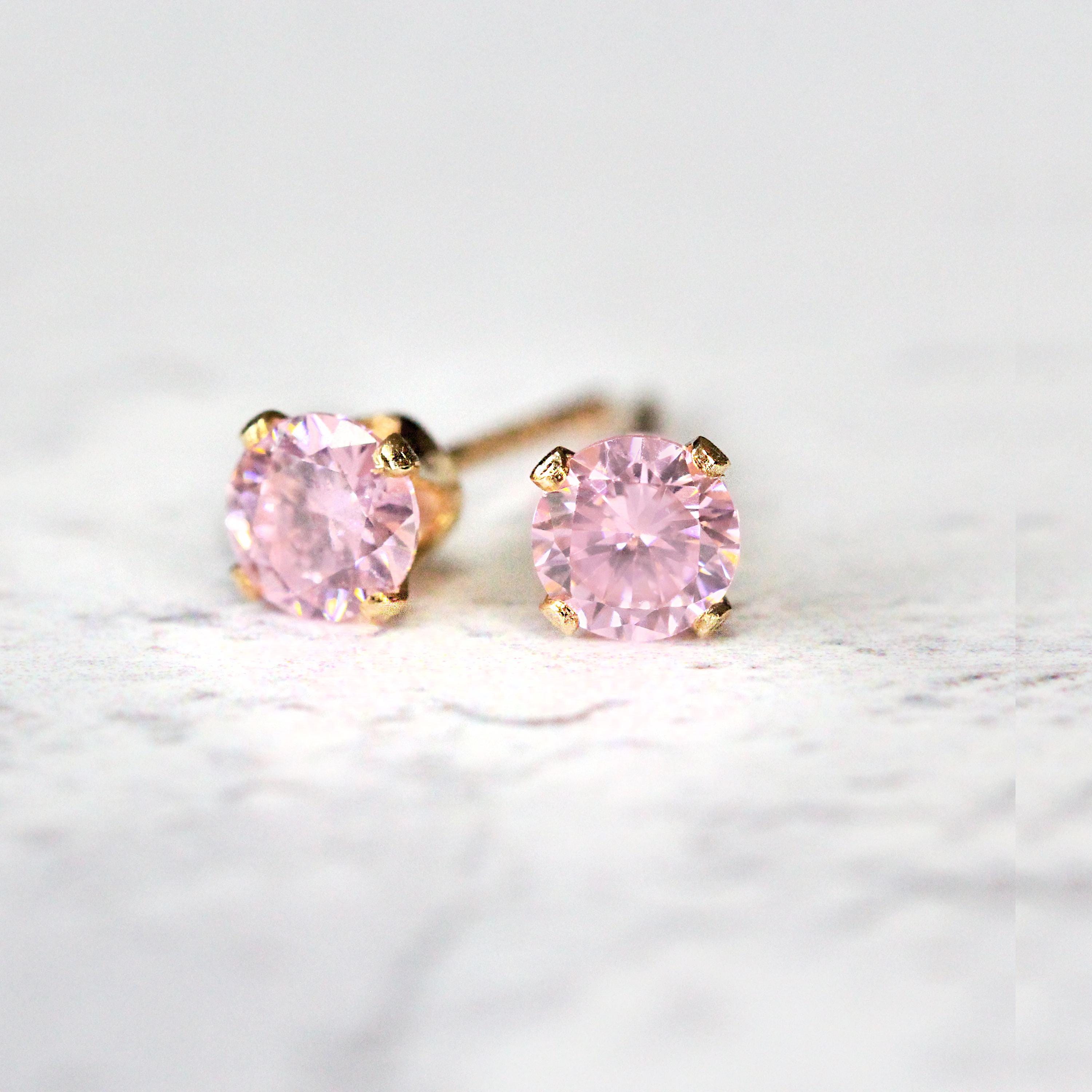 A pair of pink cubic zirconia stud earrings. The cz crystal stone is round in shape with a sparkling faceted cut. The 14k gold fill ear post setting has four prongs holding the gemstone in place, and butterfly push backs to secure the stud on the ear.