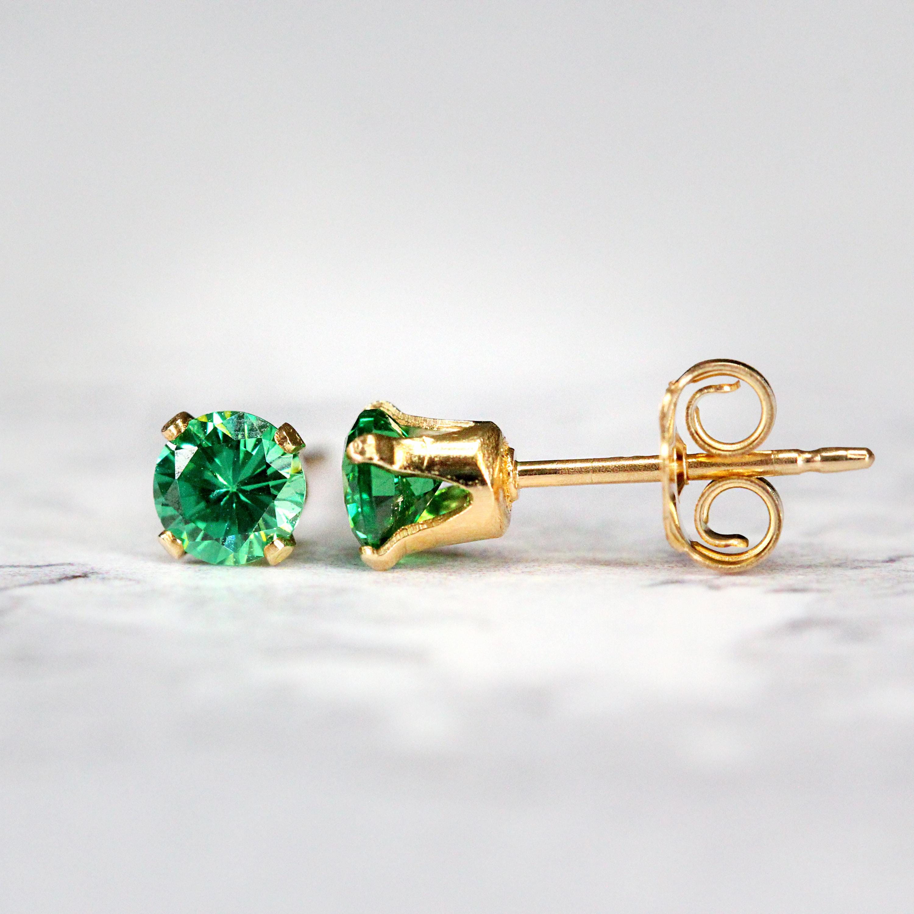 A pair of bright teal green cubic zirconia crystal gemstone stud earrings. The cz gemstones are sparkling and catch the light. The stones are a brilliant round cut with lots of facets, and set into gold fill four prong settings. Simple, minimal, round stud earrings shown against a simple light background.