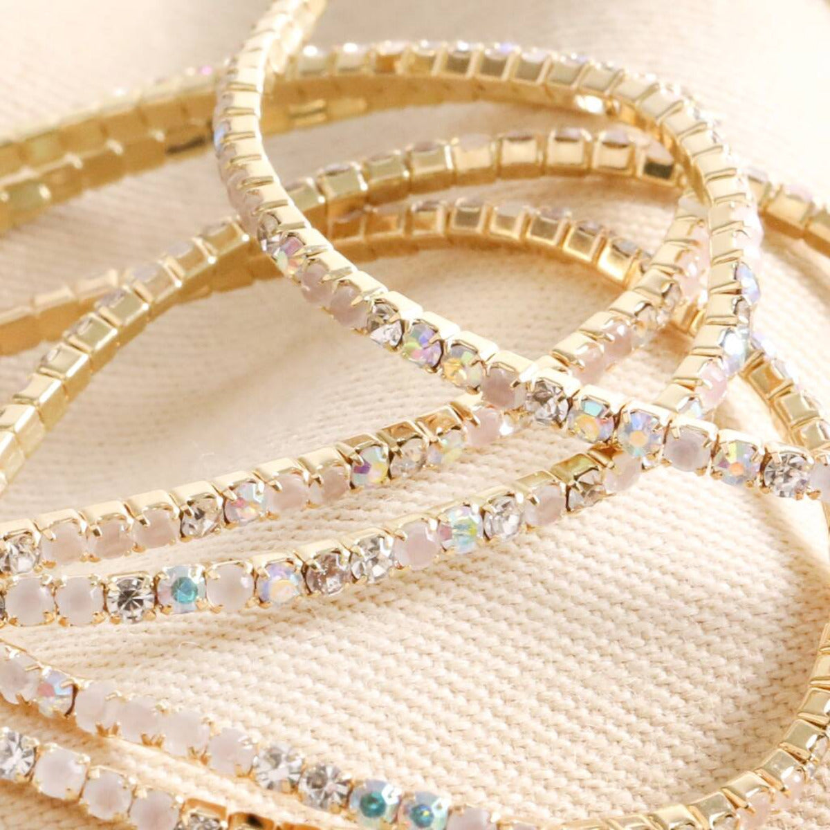 Close up of a set of Five Crystal Tennis Bracelets In Gold on a fabric background.
