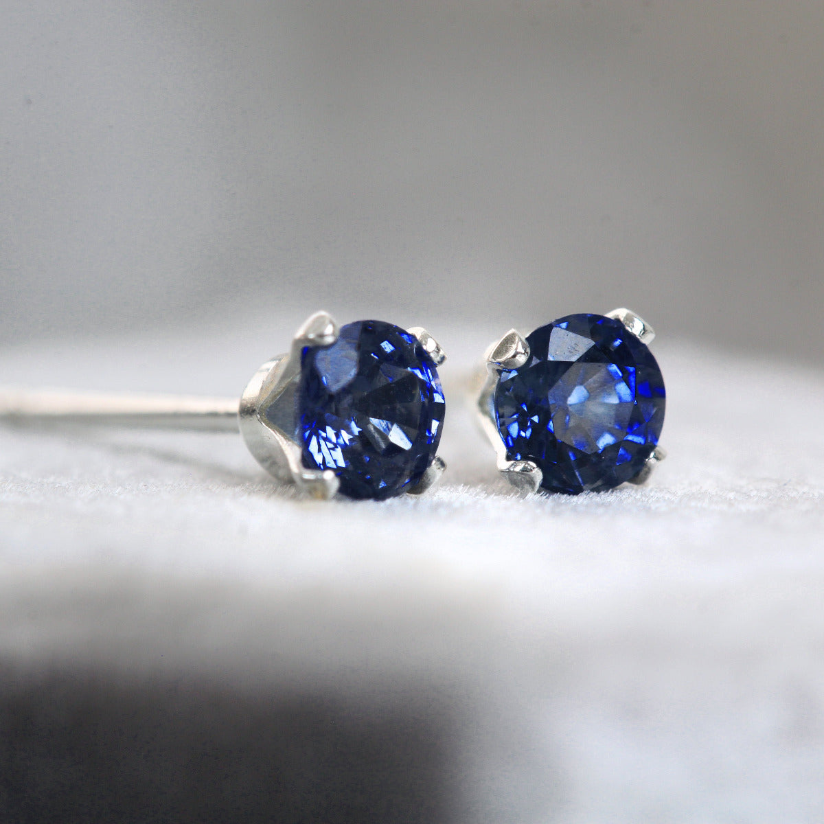 Pair of silver sapphire gemstone stud earrings on a gray background