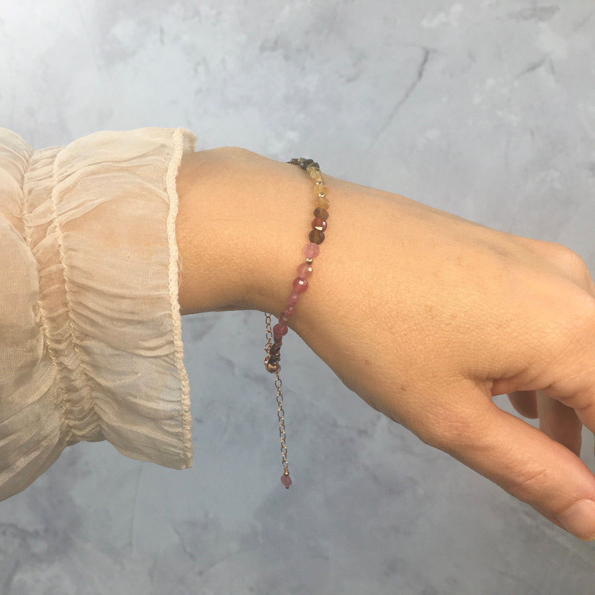 Close-up of a wrist wearing a pink and green tourmaline bead bracelet against a neutral background